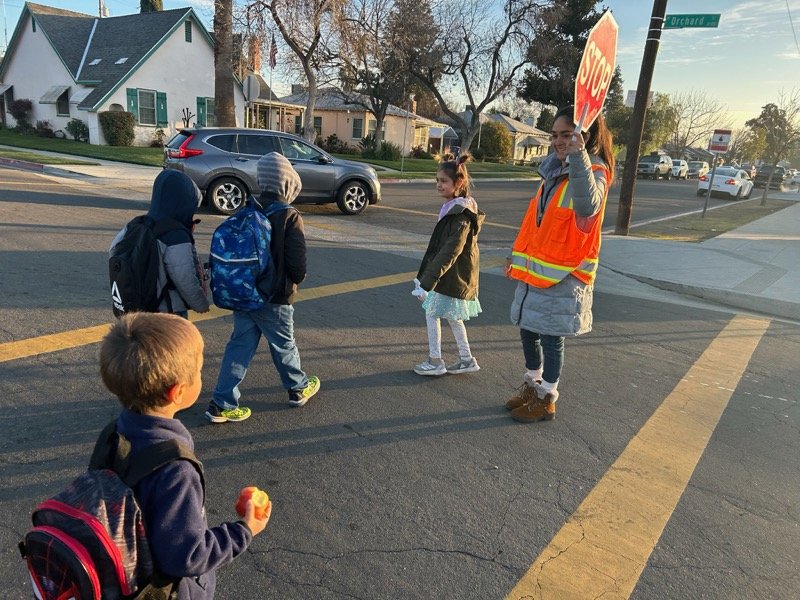A crossing guard in a high-visibility vest holding a stop sign while children cross the street on their way to school